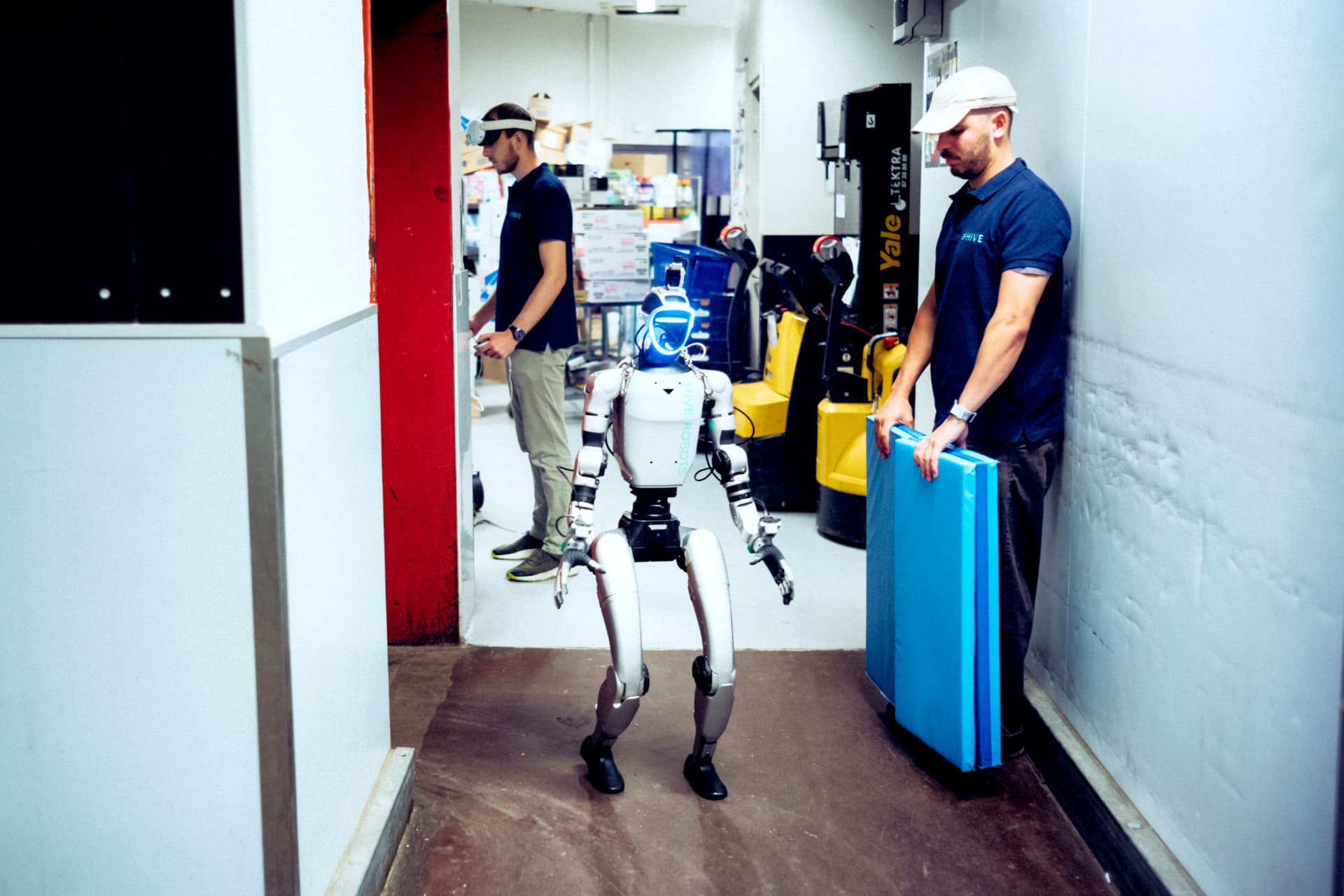 HIVE team supervising a humanoid robot with a protective mat beside its work area