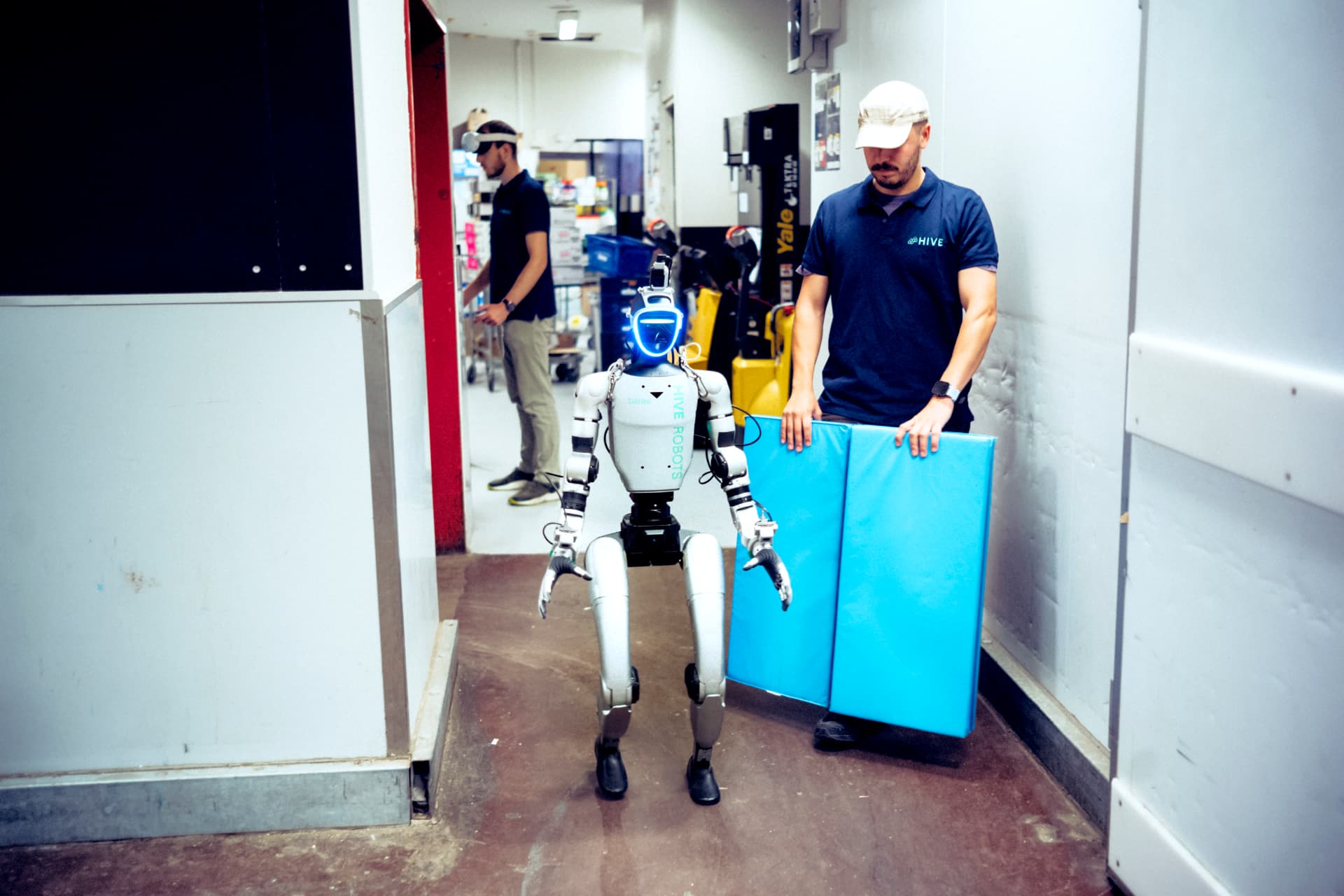 HIVE team member holding a protective mat beside a humanoid robot during training